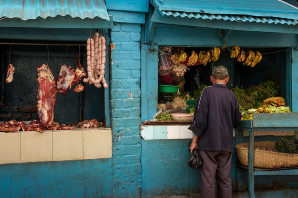 A colorful but dirty grocery store features  fresh meat hanging